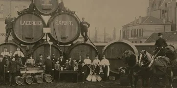 Photographie vintage en noir et blanc montrant des ouvriers devant de grandes barriques de bière marquées 'Lagerbier Export', représentant une ancienne brasserie.